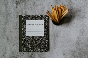 A notebook site beside a mug of freshly sharpened pencils
